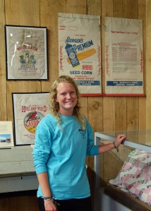 Emily in the Dubois County Museum standing under a Burger paper seed corn bag. Seed production and sales were part of the Burger farm business
